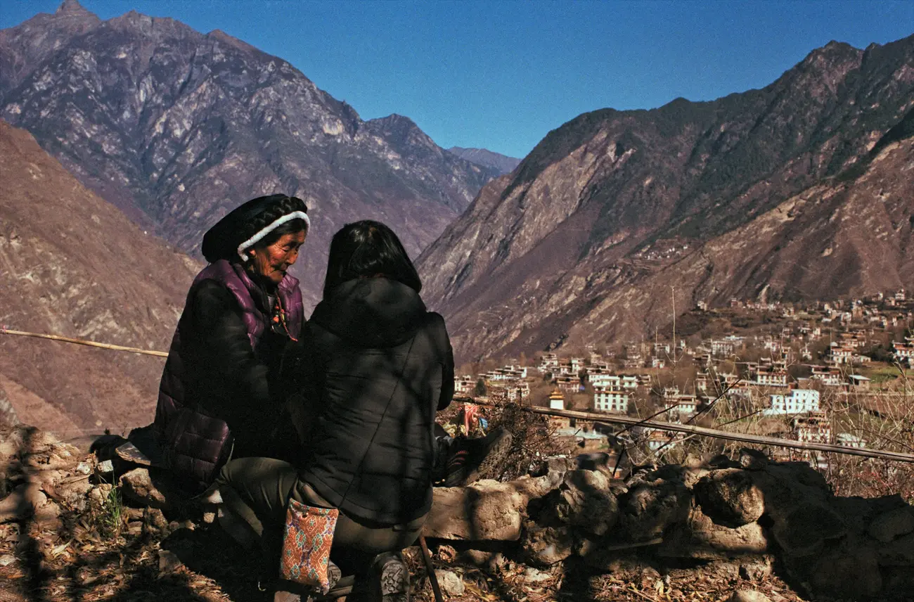 Grandma Xiage-achong chats with producer Liyuan on a cliff overlooking Zhonglu village.