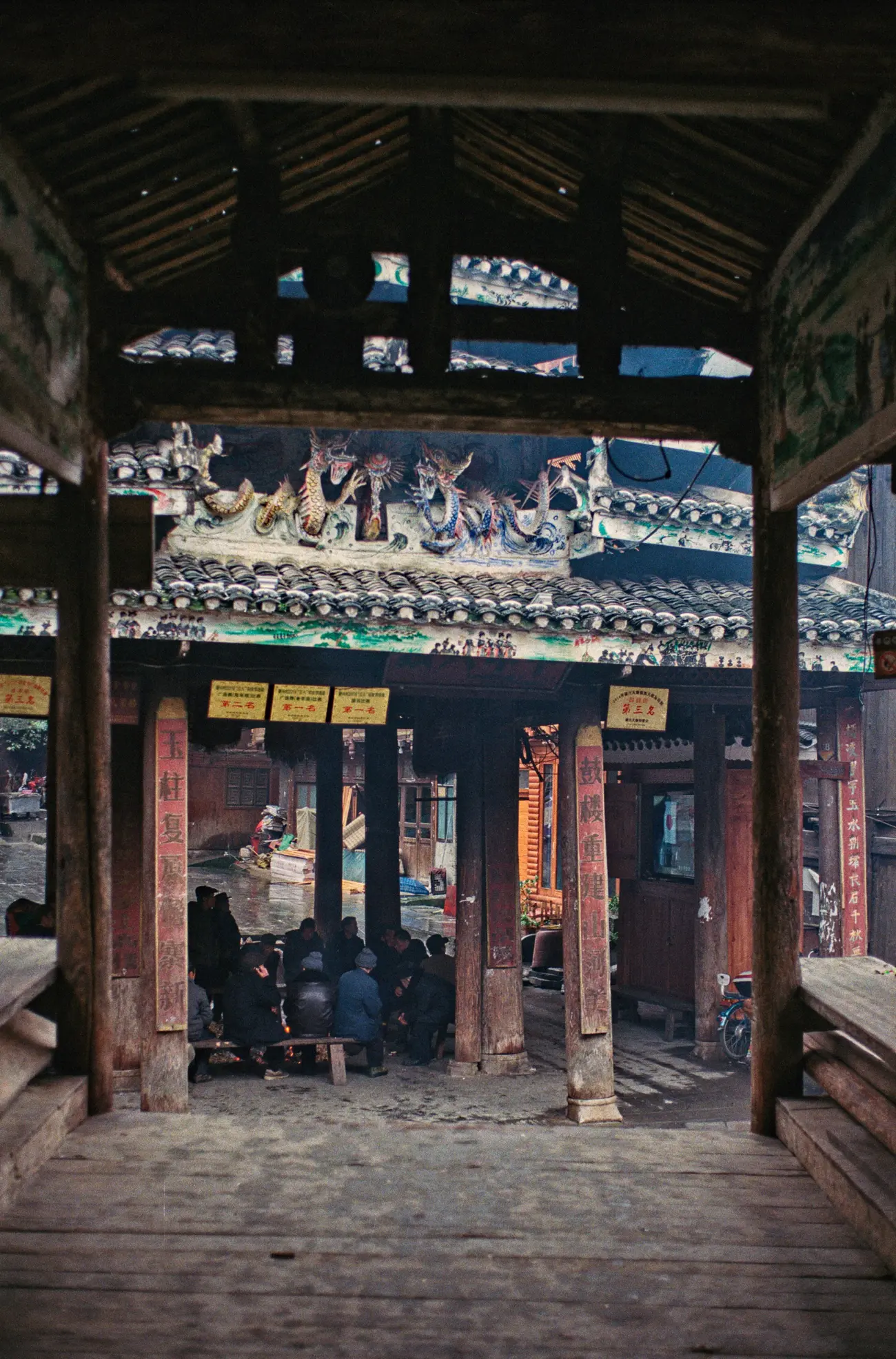 Local men huddle around a drum tower fire, watching a giant TV.
