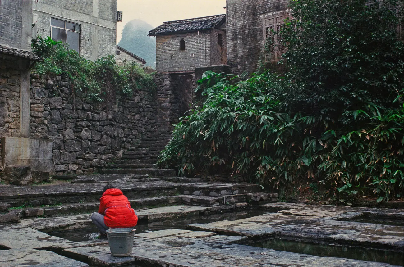 A woman does laundry in water pools at the edge of the village.
